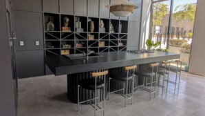 Uma cozinha moderna com uma ilha central, banquetas de bar e um armário embutido com objetos decorativos.