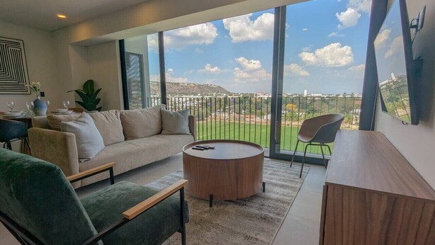 Un salon moderne comprenant un canapé, un fauteuil, une table basse et offrant une vue sur un paysage verdoyant grâce à de grandes fenêtres.
