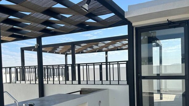 A rooftop terrace with a built-in kitchen area, a glass door, and a metal railing. - Nuevo Depa Santa Ana 360 - 40 (Torre 11) (Zapopan)
