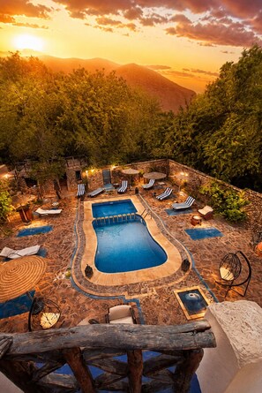 A pool area with lounge chairs and umbrellas, surrounded by stone walls and vegetation. - Riad des Vieilles Charrues (Ait Sedrate Jbel El Soufla)