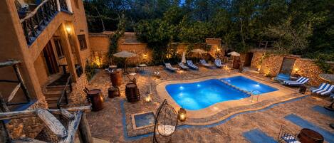 A pool area with stone flooring, lounge chairs, and a stone wall.