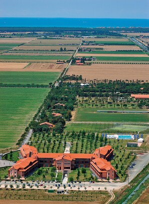 Eine Vogelperspektive auf einen großen Gebäudekomplex mit mehreren Gebäuden mit roten Dächern, umgeben von grünen Feldern und einer Straße.