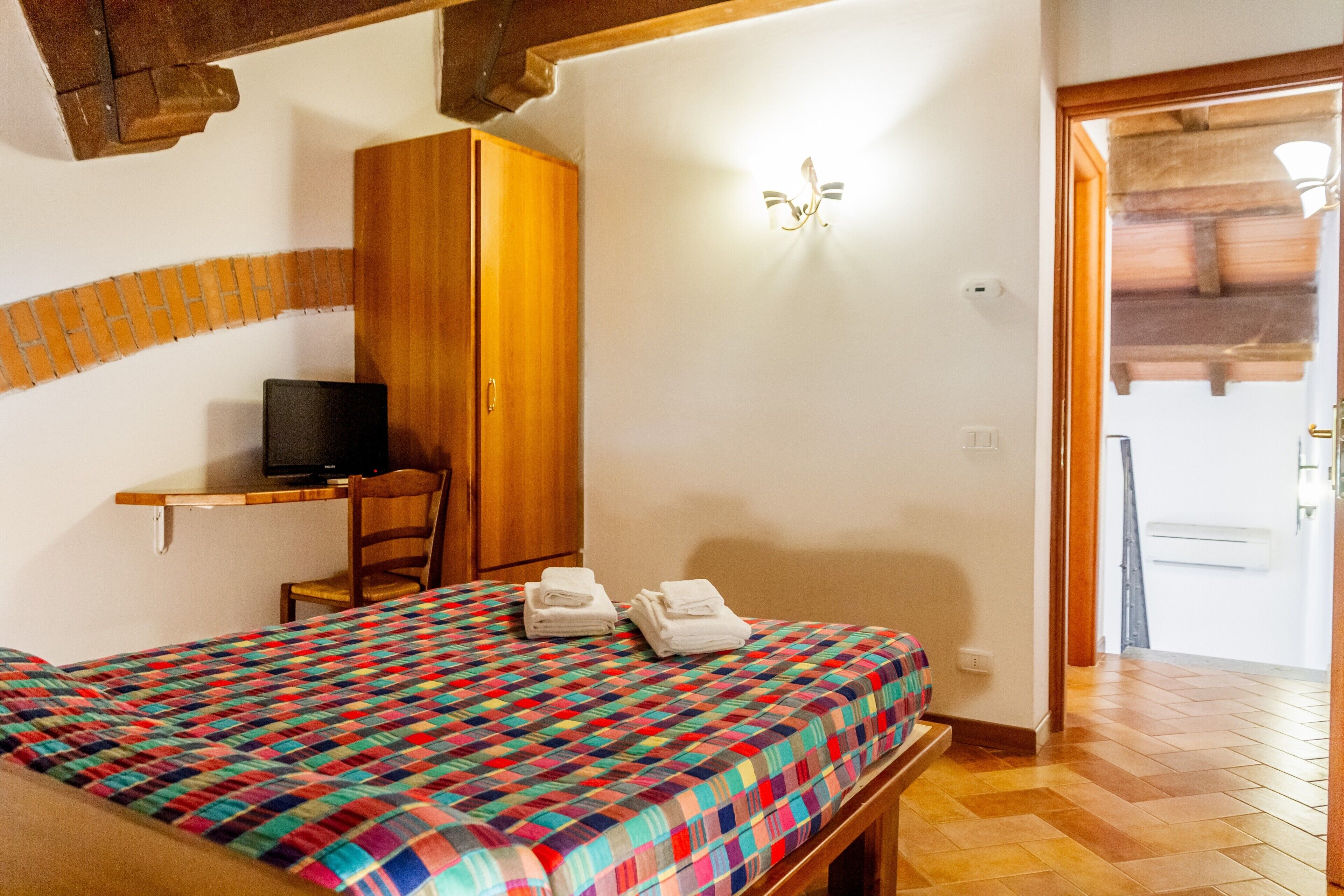 A bedroom with a bed, a television on a shelf, a wardrobe, and a door leading to another room.