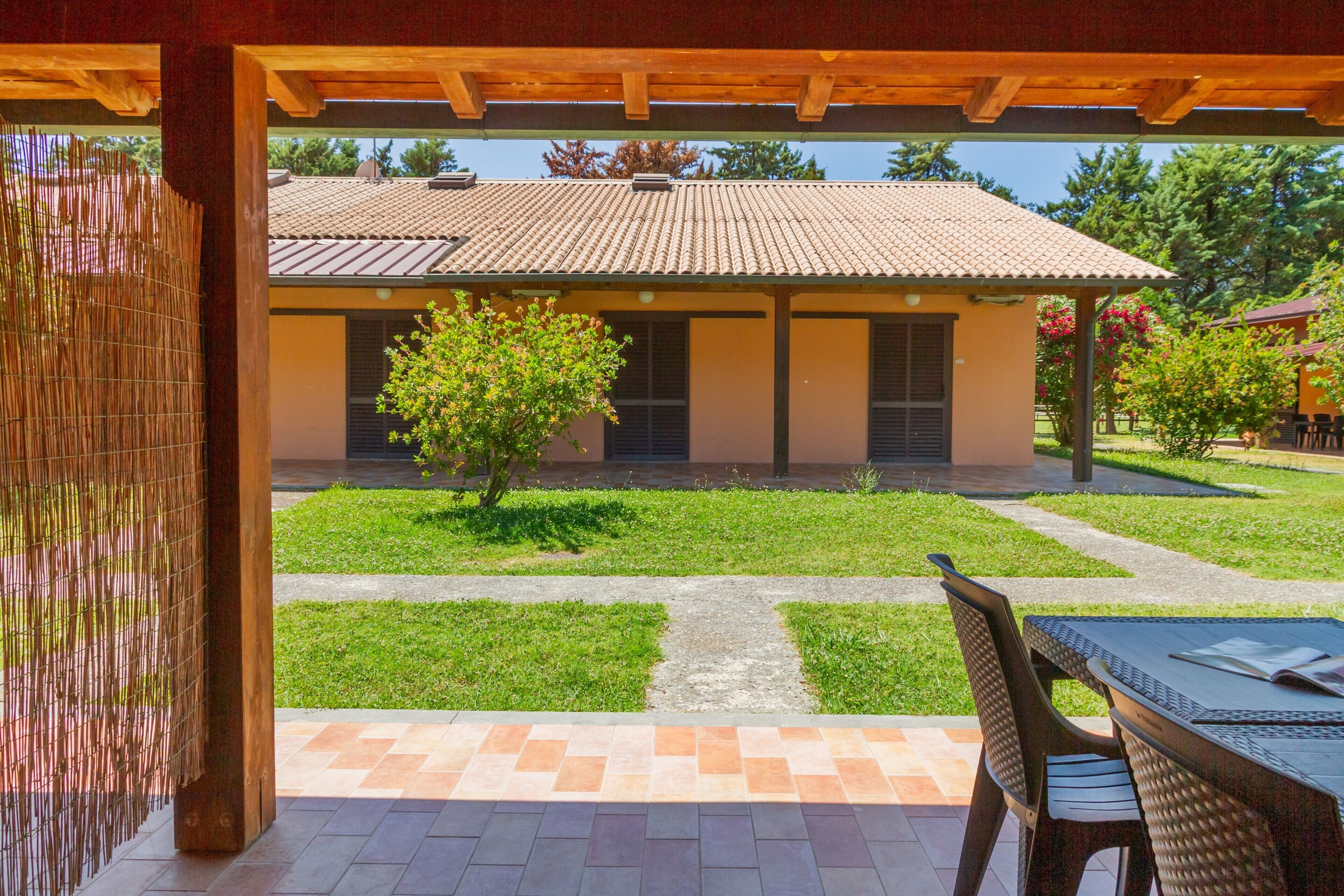 Un patio couvert avec une table et des chaises, un petit arbre et, au fond, un bâtiment doté d’un toit en tuiles.
