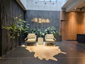Ein Empfangsbereich im modernen Design mit einer Holzwand, auf der der Name 'ATENA' beleuchtet ist, zwei Ledersesseln, einem runden Couchtisch und einem Kuhfellteppich.