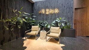 Een modern interieur met twee leren fauteuils, een ronde salontafel, en een bordje aan de muur met de tekst 'ATENA'.