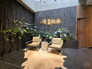 Ein modernes Interieur mit zwei Ledersesseln, einem runden Couchtisch und einem an der Wand befestigten Schild mit der Aufschrift 'ATENA'.