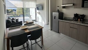 Une cuisine moderne équipée d’un four encastré, d’un four à micro-ondes et d’une machine à café. On y trouve également un coin repas avec une table et des chaises, ainsi qu’une grande fenêtre donnant sur l’extérieur.