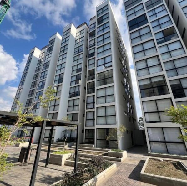 A modern high-rise building with multiple floors, large windows, and a courtyard with planters.