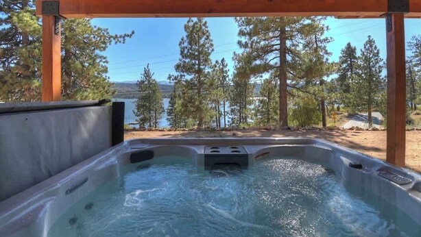 Un bain à remous installé sous une pergola en bois, offrant une vue sur les arbres et un plan d’eau.