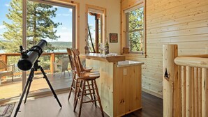 Une cabane en bois dotée de grandes fenêtres, d’un télescope et d’un coin bar.