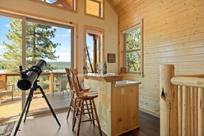 A wooden cabin with large windows, a telescope, and a bar area. - New Lakefront Retreat w/ Hot Tub & Game Room (Fawnskin)