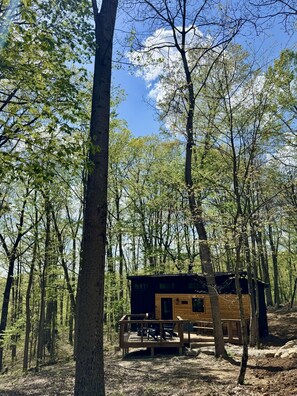 A cabin in a forest with a deck and outdoor seating.