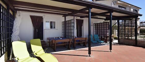 Une terrasse extérieure couverte, avec une table et des chaises, une pergola et un espace délimité par une clôture.