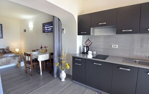 A modern kitchen with dark cabinets, a dining area with a table and chairs, and a flat-screen TV mounted on the wall. - Cozy Beachside Retreat (Umag)