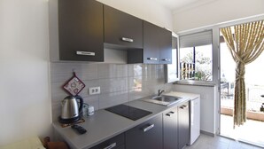 A modern kitchen with dark cabinets, a kettle, a remote, and a window with curtains. - Compact Studio Stay With sea Views and BBQ (Umag)