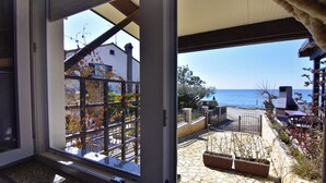 A view through a window of a patio area with a stone floor, outdoor furniture, and a view of the sea. - Compact Studio Stay With sea Views and BBQ (Umag)