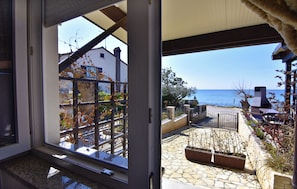 A view through a window of a patio area with a stone floor, outdoor furniture, and a view of the sea. - Compact Studio Stay With sea Views and BBQ (Umag)