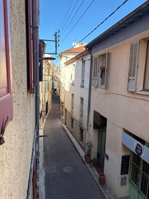 Un carrer estret amb edificis a ambdós costats, una tapa de clavegueram visible i un senyal amb la paraula 'MOON' a la dreta.