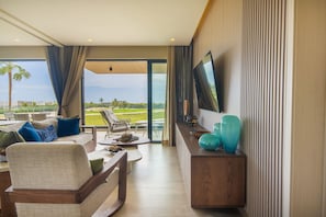 A modern living room with a sofa, a coffee table, a TV, and a view of a golf course. - Vermare Cap Cana | Golf, Pool and Luxury (punta cana)