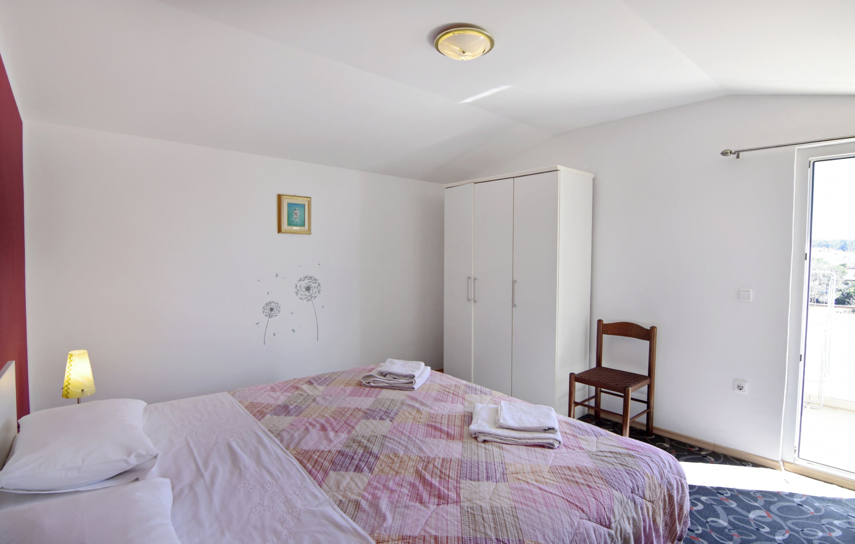 Een slaapkamer met een bed, een stoel, een kledingkast en een raam.