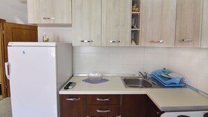 A kitchen with wooden cabinets, a white refrigerator, a sink, and a dish drying rack. - Practical Stay With Ocean View (Umag)