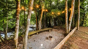 Un espace boisé avec un banc en bois, un foyer et des guirlandes lumineuses.