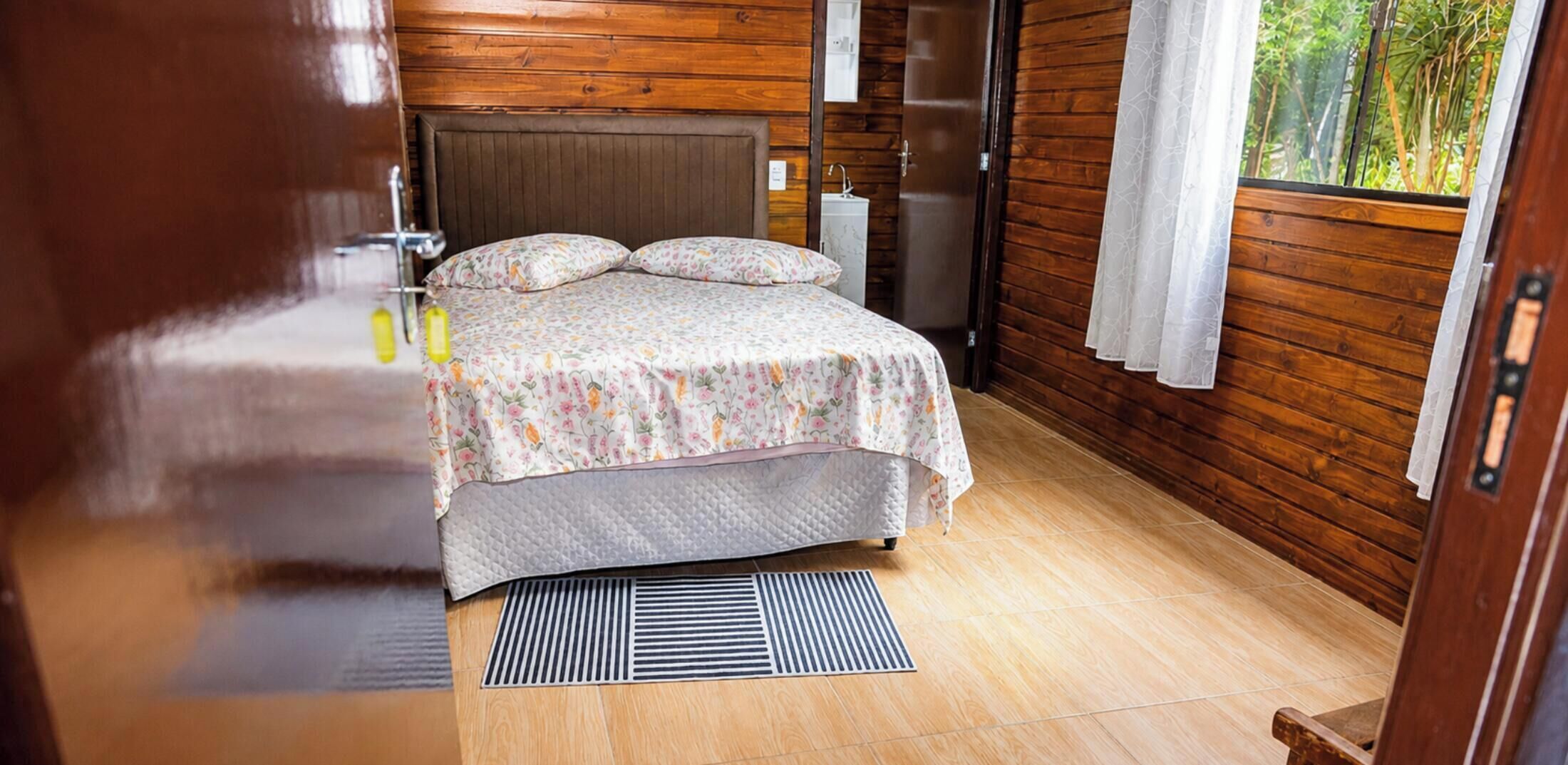 Una habitación con paneles de madera, una cama, un radiador y una ventana con cortinas.