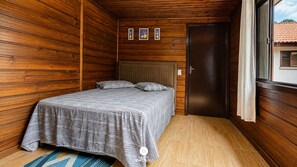A bedroom with a bed, wooden walls, a door, and a window with curtains. - Sítio Conteiner do Mano - Águas Mornas (Águas Mornas)
