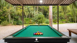 A pool table with a green felt surface, surrounded by a covered area with a view of a forested area. - Sítio Conteiner do Mano - Águas Mornas (Águas Mornas)