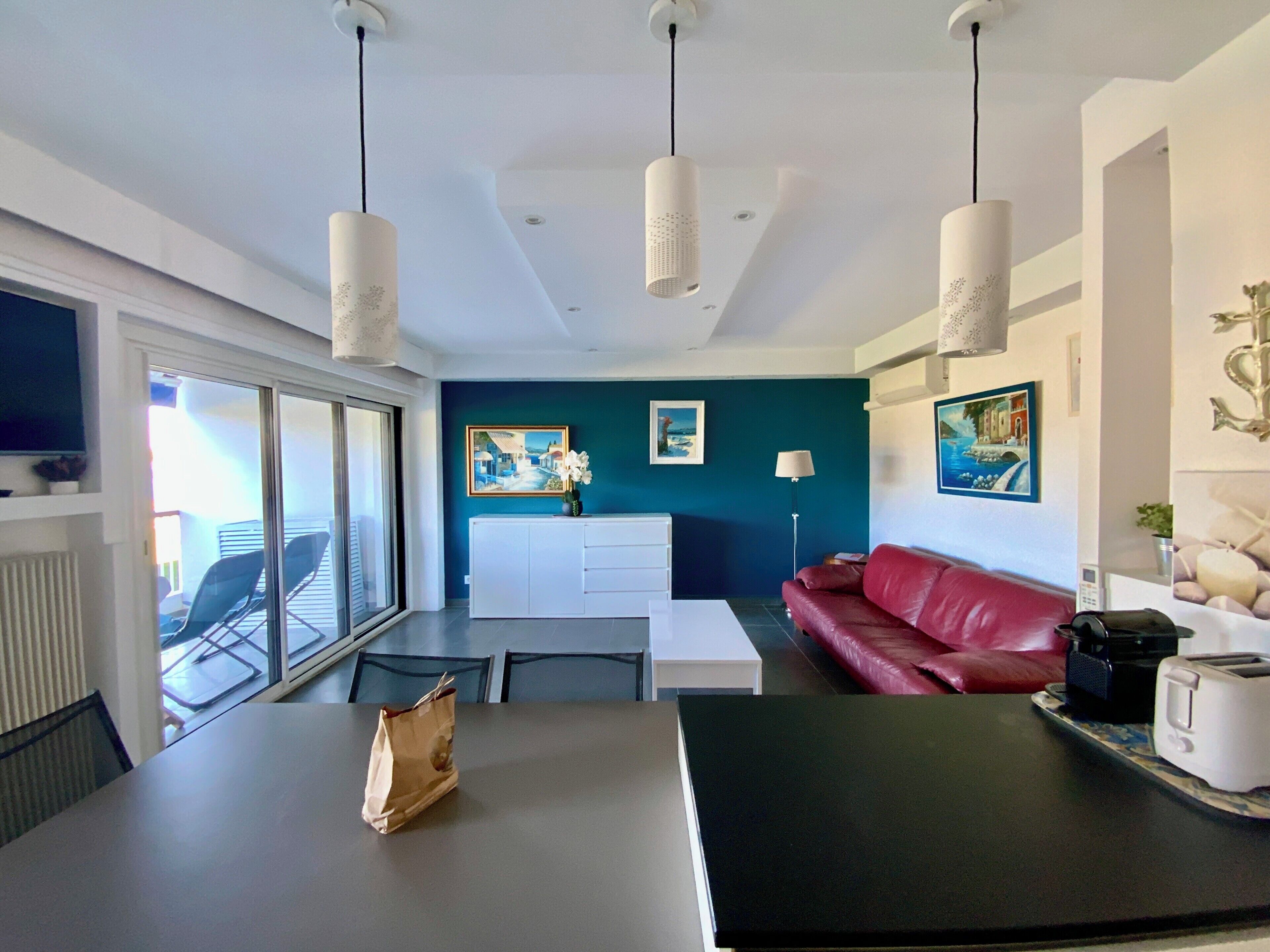 Ein modernes Wohnzimmer mit einem roten Sofa, einem weißen Esstisch und einer Küchenzeile.