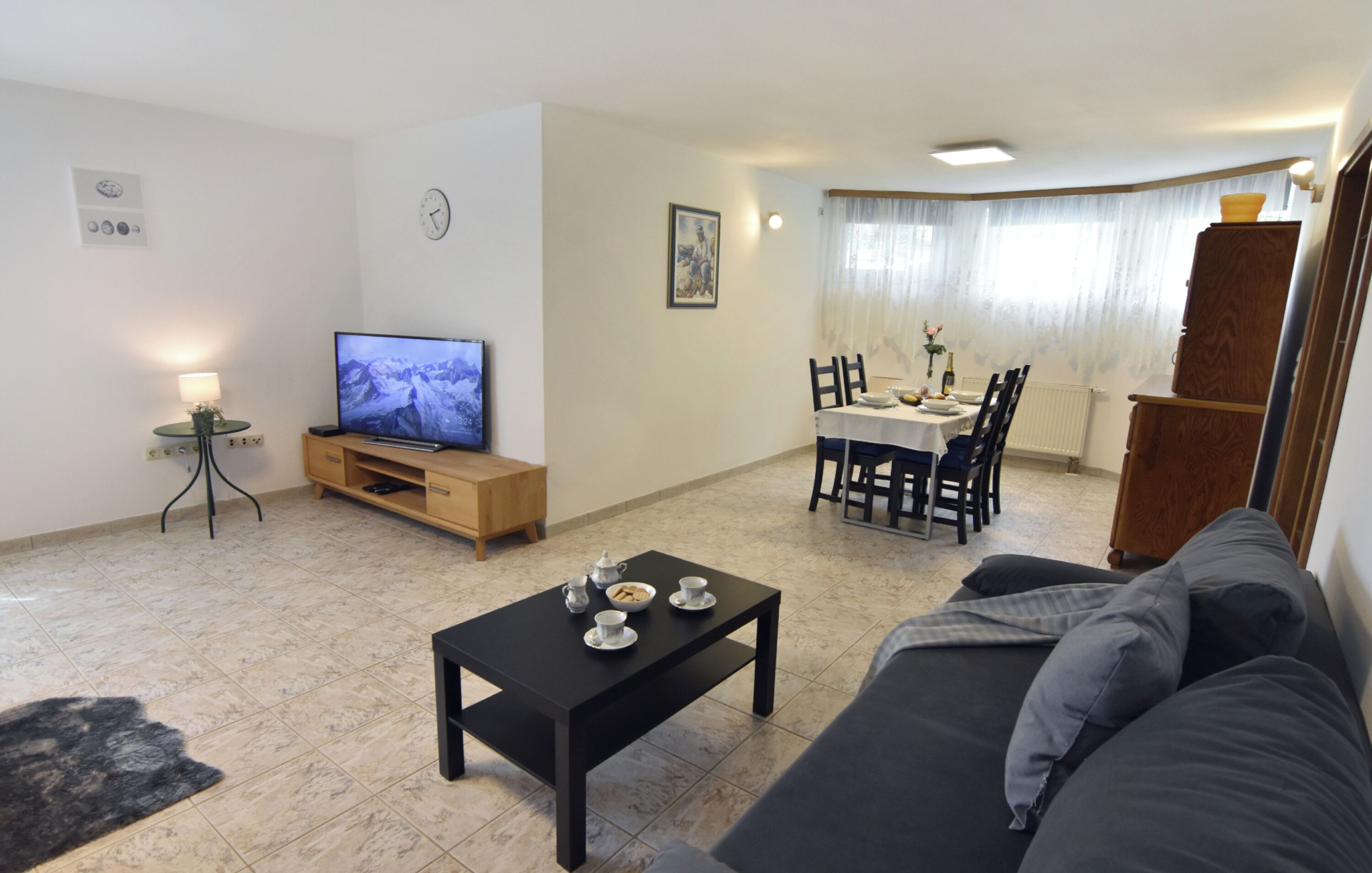 A living room with a TV, a coffee table, a sofa, and a dining area with chairs and a table.