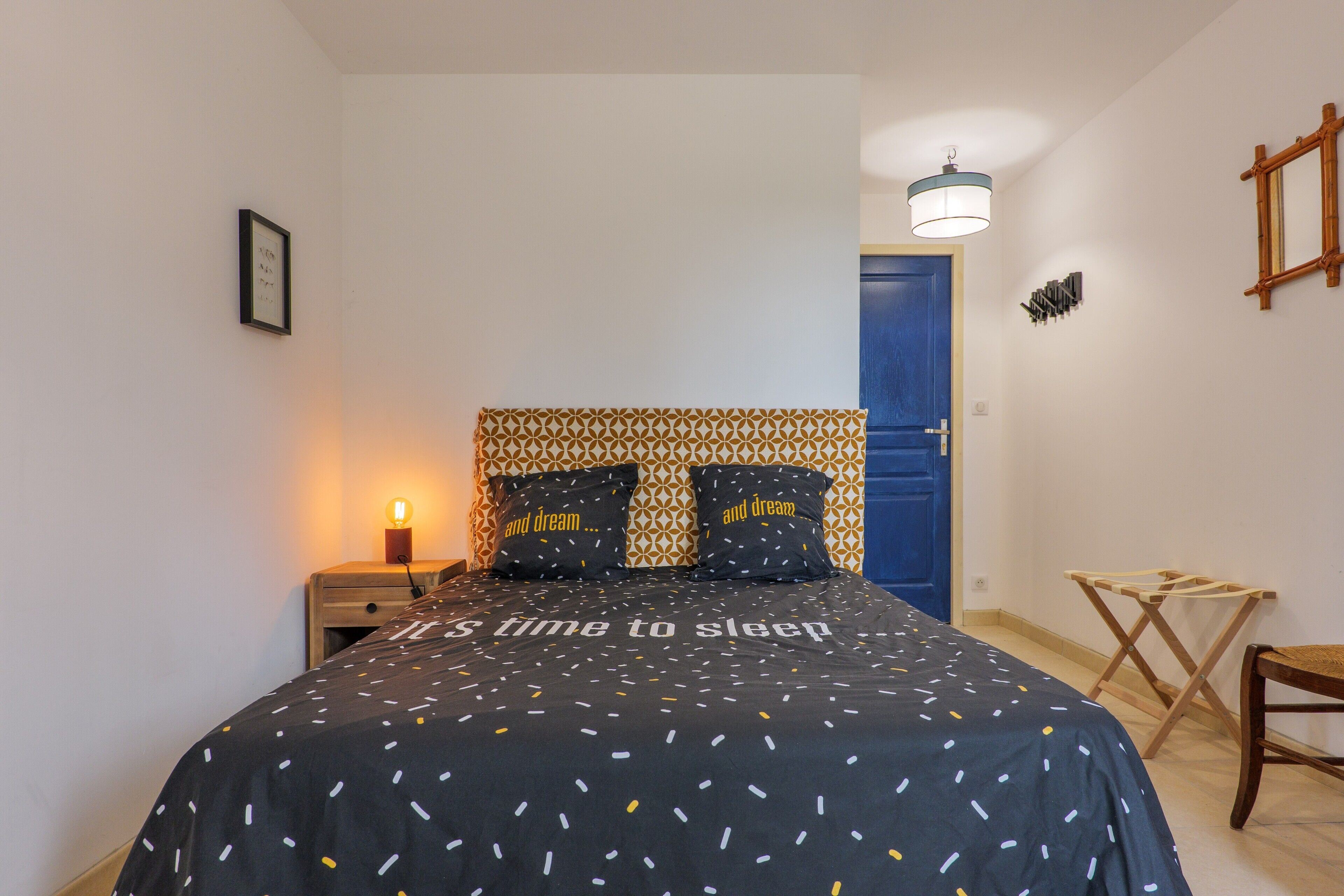 Een slaapkamer met een bed, een bedlampje en een blauwe deur.