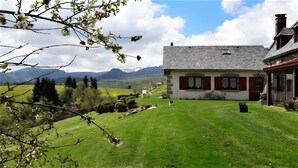 Una casa con tetto spiovente, un prato e vista sulle montagne sullo sfondo.