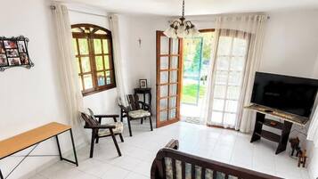 Una habitación con televisión, un banco, dos sillas, una mesita y una puerta que da al exterior.