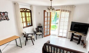 A room with a television, a bench, two chairs, a small table, and a door leading outside.