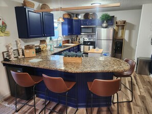 Eine Küche mit dunkelblauen Schränken, einer Granitinsel mit Barhocker, Edelstahlgeräten und Holzboden.