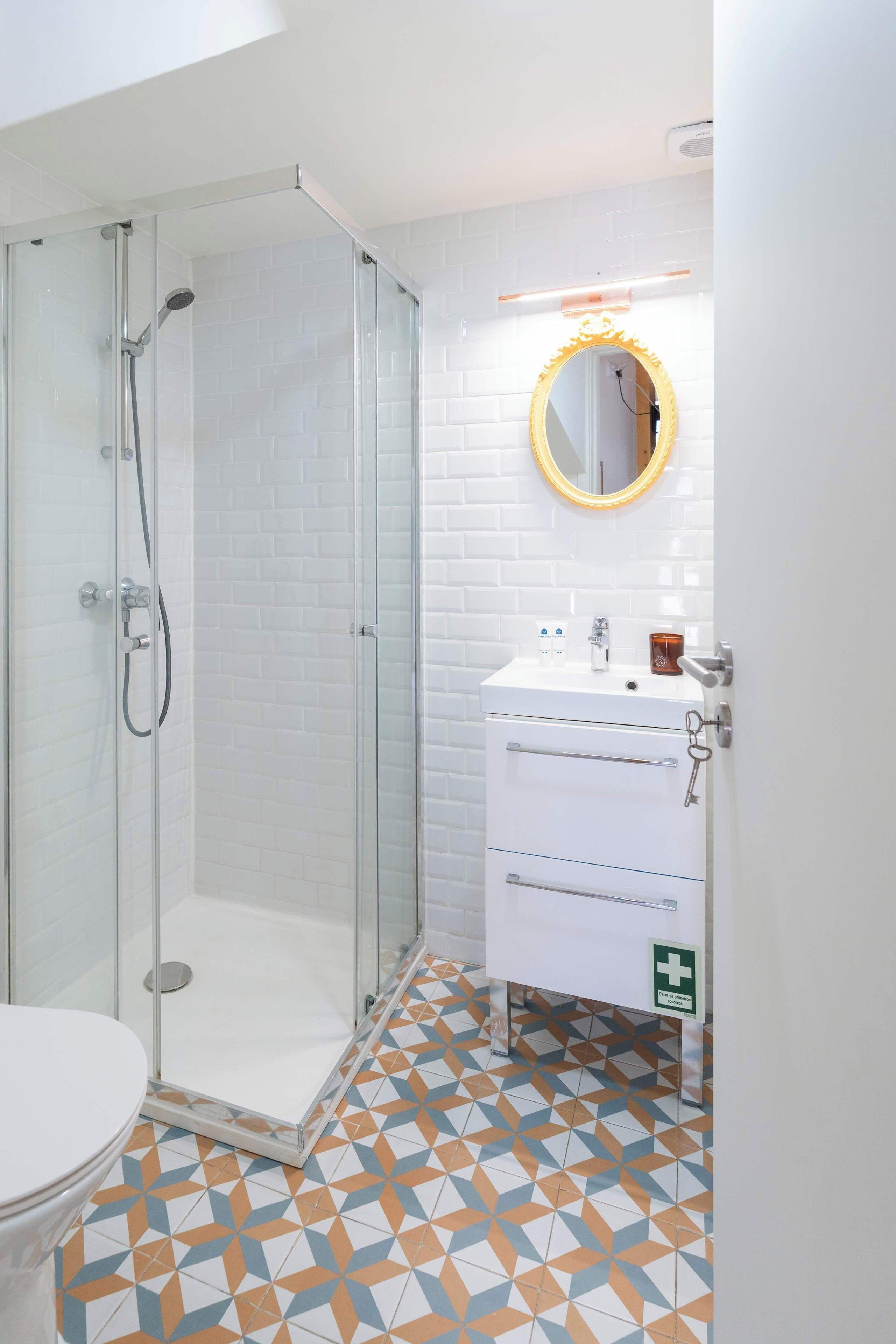 A bathroom with a glass-enclosed shower, a white sink with a mirror, and a patterned floor.