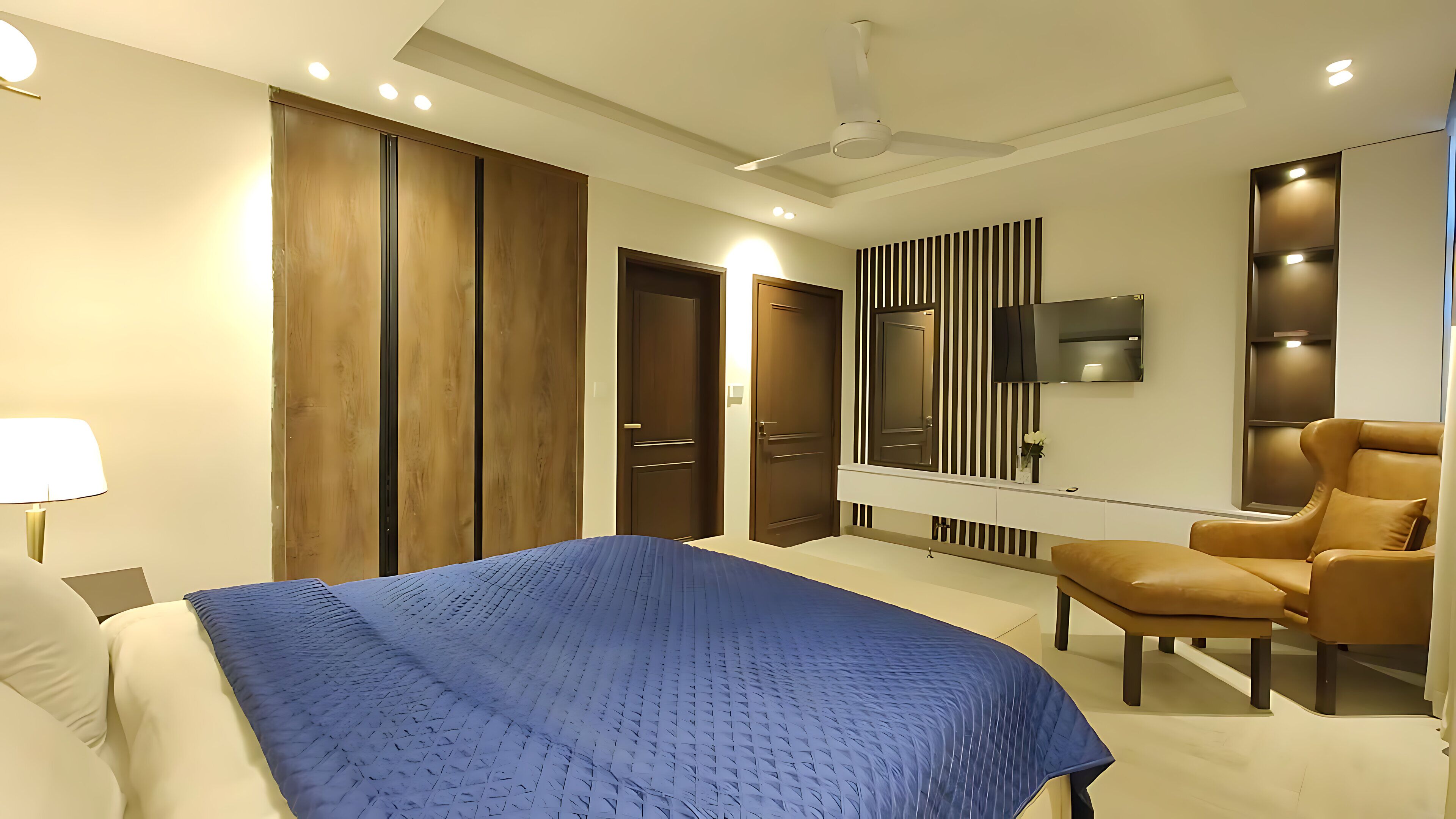 A modern bedroom with a bed, a chair, a TV, and a ceiling fan.