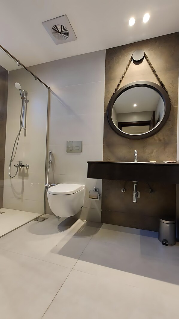 A modern bathroom with a glass shower enclosure, a toilet, a sink with a mirror, and a trash bin.