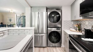 Eine kompakte Küche mit Edelstahl-Kühlschrank, integriertem Wasch- und Trockner, schwarzem Backofen und weißer Arbeitsplatte.