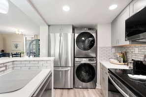 A compact kitchen with a stainless steel refrigerator, a built-in washer and dryer, a black oven, and a white countertop.