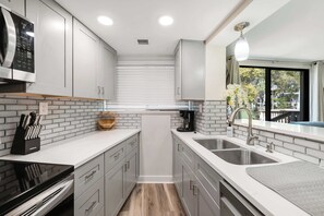 A modern kitchen with white cabinets, a black stove, a double sink, and a window with a view.