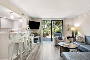 A modern kitchen with a bar area, a flat-screen TV, and a dining table with chairs.