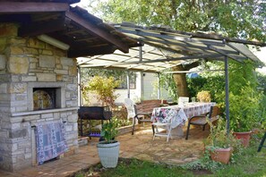 A stone building with a fireplace, a covered patio with chairs and a table, and potted plants. - Elegant Living for Your Vacation (Umag)