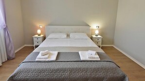 Un lit bien fait, recouvert d’une couette grise, deux tables de chevet avec des lampes et un mur de couleur claire.