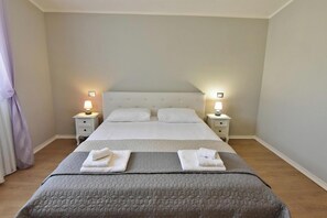 A neatly made bed with a grey quilt, two bedside tables with lamps, and a light-colored wall. - Elegant Living for Your Vacation (Umag)
