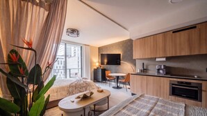 A modern hotel room with a bed, a small dining table, a kitchen area, and a large window. - Bright apartment w/ pool & workspace (Miami)