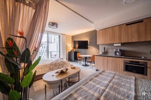 A modern hotel room with a bed, a small dining table, a kitchen area, and a large window. - Bright apartment w/ pool & workspace (Miami)