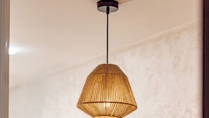 A pendant light fixture with a woven design, wooden shelves with decorative items, and a textured wall. - Comfortable apartment in the heart of Guéliz (Marrakech)